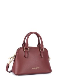 Petit sac à main en cuir bordeaux avec deux poignées, fermeture éclair dorée, bandoulière amovible et logo "Lancaster Paris" à l'avant.