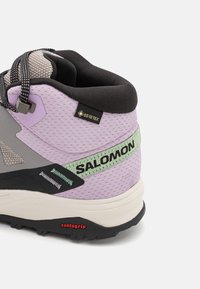 Chaussures de randonnée violettes et grises avec tissu en mesh, talon renforcé et accents noirs. Présente un logo "SALOMON" vert et une semelle extérieure Contagrip.