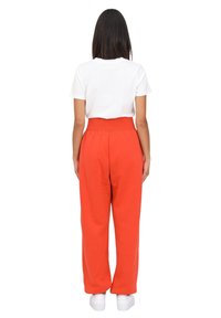 Pantalones deportivos rojos de talle alto con un corte relajado, combinados con una camiseta blanca de manga corta. Zapatillas blancas completan el atuendo.