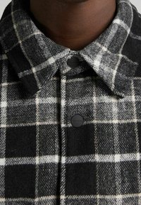 Svart och vit rutig skjorta med en tjock ullstruktur, med en knapp-down krage och svarta knappar med logodetalj.