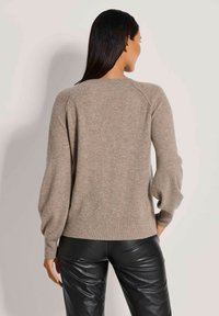 Beige gestrickter Pullover mit Rundhalsausschnitt und Ballonärmeln, mit gerippten Akzenten an den Manschetten und dem Saum. Kombiniert mit schwarzen Lederhosen.