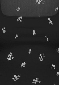 Tissu noir avec de petites impressions florales blanches dispersées uniformément sur la surface et une zone texturée plus foncée près du haut.