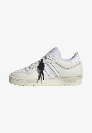 Basket basse blanche Adidas avec trois bandes, panneaux en mesh et un détail de lacet noir noué unique sur le côté.