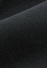 Crni pleteni materijal s glatkom teksturom. Ima blagi sjaj, a materijal prikazuje ravnotežnu šav i nema vidljivih uzoraka ili akcenta.