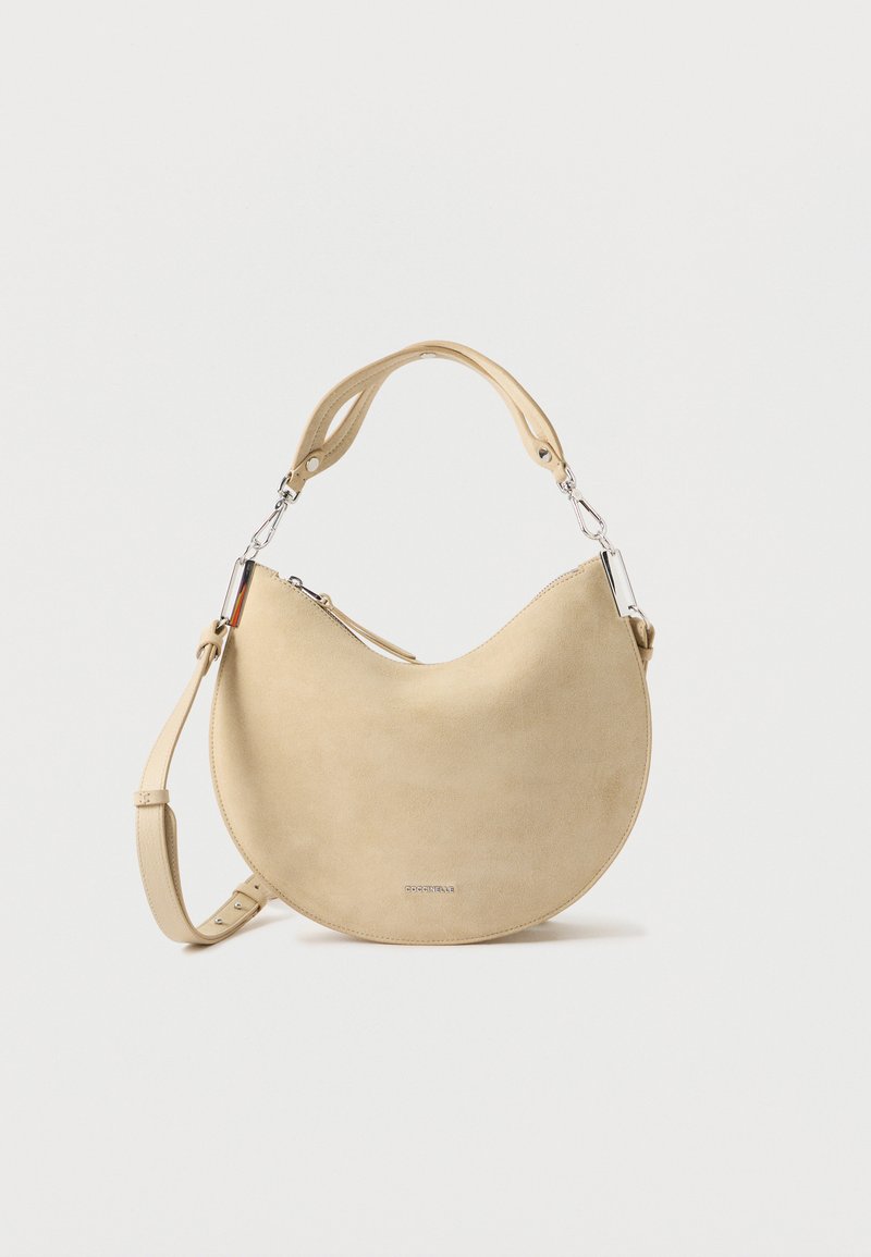 Beige suède schoudertas met een gebogen vorm, verstelbare riem en metalen hardware accenten. Gladde textuur met minimale ontwerpdetails.