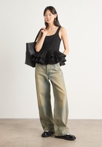 Čierny peplum top s volánom na spodnom okraji, skombinovaný s voľnými svetlomodrými džínami a čiernymi platformovými topánkami; model drží čiernu tote tašku.