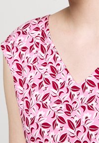 Růžové květinové šaty s výstřihem do V a krátkými rukávy, s motivem listů a květin v odstínech červené a bílé na růžovém pozadí.