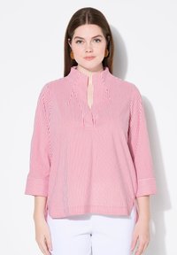 Camicia a righe con strisce verticali rosse e bianche, con un collo alto e uno spacco, e maniche a tre quarti con polsini. Tessuto morbido.