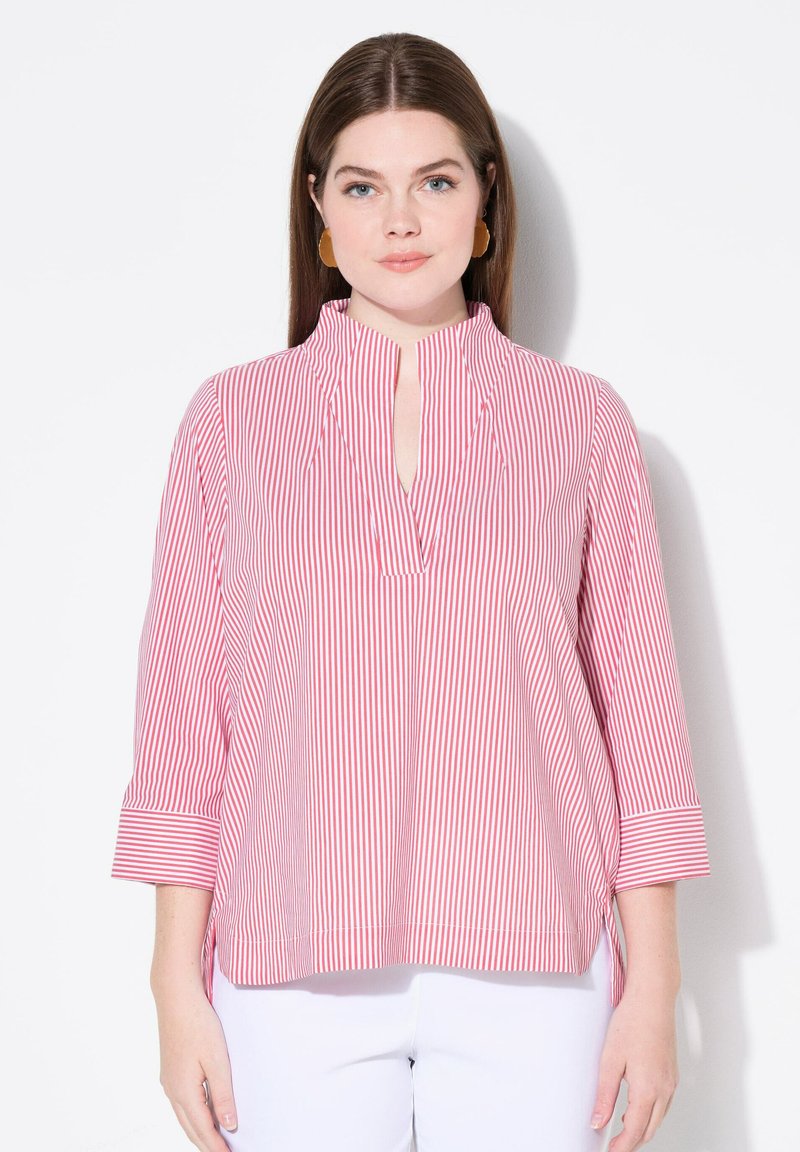 Camicia a righe con strisce verticali rosse e bianche, con un collo alto e uno spacco, e maniche a tre quarti con polsini. Tessuto morbido.