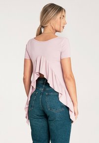 Jasnoróżowa bluzka z falbanką na plecach, krótkimi rękawami i okrągłym dekoltem, zestawiona z wysokimi dżinsami. Gładka faktura materiału.