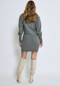 Abito maglione grigio con maniche a coste e orlo a coste, abbinato a stivali in pelle beige alti fino al ginocchio. Tessuto morbido e design aderente.