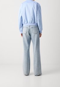 Jasnoniebieska kurtka bomber z prążkowanymi mankietami, zestawiona z jasnoniebieskimi rozkloszowanymi dżinsami z tylnymi kieszeniami i spranym efektem.