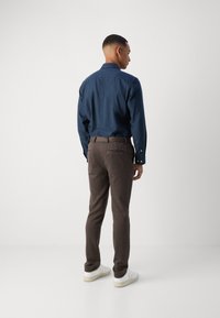 Dark blue button-up shirt with a collar, paired with brown textured pants featuring a subtle pattern and white sneakers.
