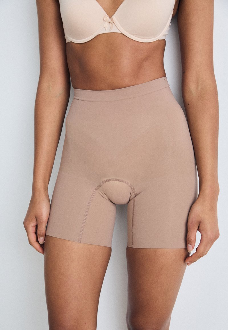 Beige high-waisted shorts in smooth, stretchy fabric with a seamless design and a central gusset for comfort and support.