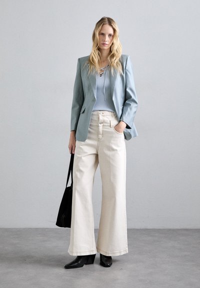 Jasnoniebieska marynarka noszona na prążkowanej jasnoniebieskiej bluzce, w zestawie z szerokimi białymi spodniami i czarnymi, wskazującymi na kostkę botkami. W komplecie czarna torba tote.