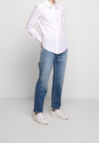 Vit skjorta med krage, i kombination med ljusblå jeans och vita sneakers. Skjortan har små dekorativa detaljer vid kragen.