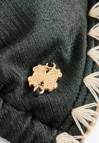 Czarna tkanina o teksturowanym wykończeniu z ozdobnymi złotymi elementami i beżowym frędzlem wzdłuż krawędzi.