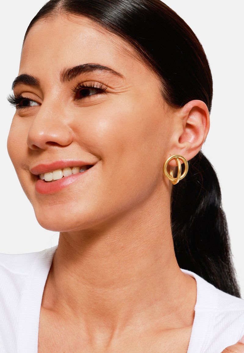 Gouden metalen oorbellen met een vloeiend, onderling verbonden lusontwerp. Gladde oppervlakken met een gepolijste afwerking versterken hun elegante uitstraling.