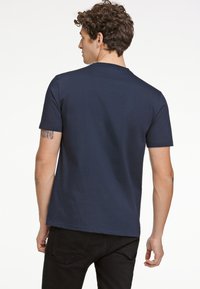 Navyblauwe T-shirt met korte mouwen van katoen, met een ronde hals en een gladde textuur. Zichtbare tatoeage op de linkerarm.