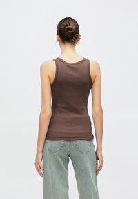 Barna pamut ujjatlan felső, testhez simuló fazonnal, kerek nyakkivágással és vékony vállpántokkal, melyet világoskék, bő szárú farmernadrággal párosítottak.