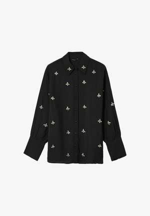 Chemise noire à manches longues avec col, ornée de broderies en forme d'abeille argentées sur l'ensemble. Fabriquée en tissu léger, elle possède des manches à poignets froncés.