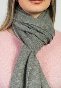 Grå scarf i mjukt, texturerat tyg, löst lindad runt halsen, med fransade kanter, tillsammans med en ljusrosa tröja.