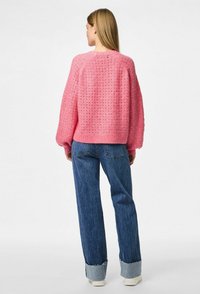 Maglione rosa a maglia con una vestibilità ampia, caratterizzato da un design testurizzato. Abbinato a jeans blu con orlo risvolto.