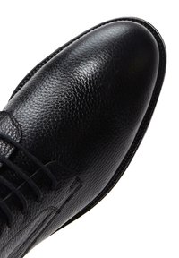 Scarpa in pelle nera con finitura testurizzata, punta rotonda e lacci intatti. Presenta una suola liscia e cuciture sottili lungo i bordi.