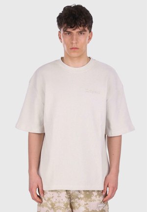 Overdimensioneret cremefarvet ribbede bomulds T-shirt med korte ærmer, prydet med et diskret broderet logo på brystet og en afslappet pasform.