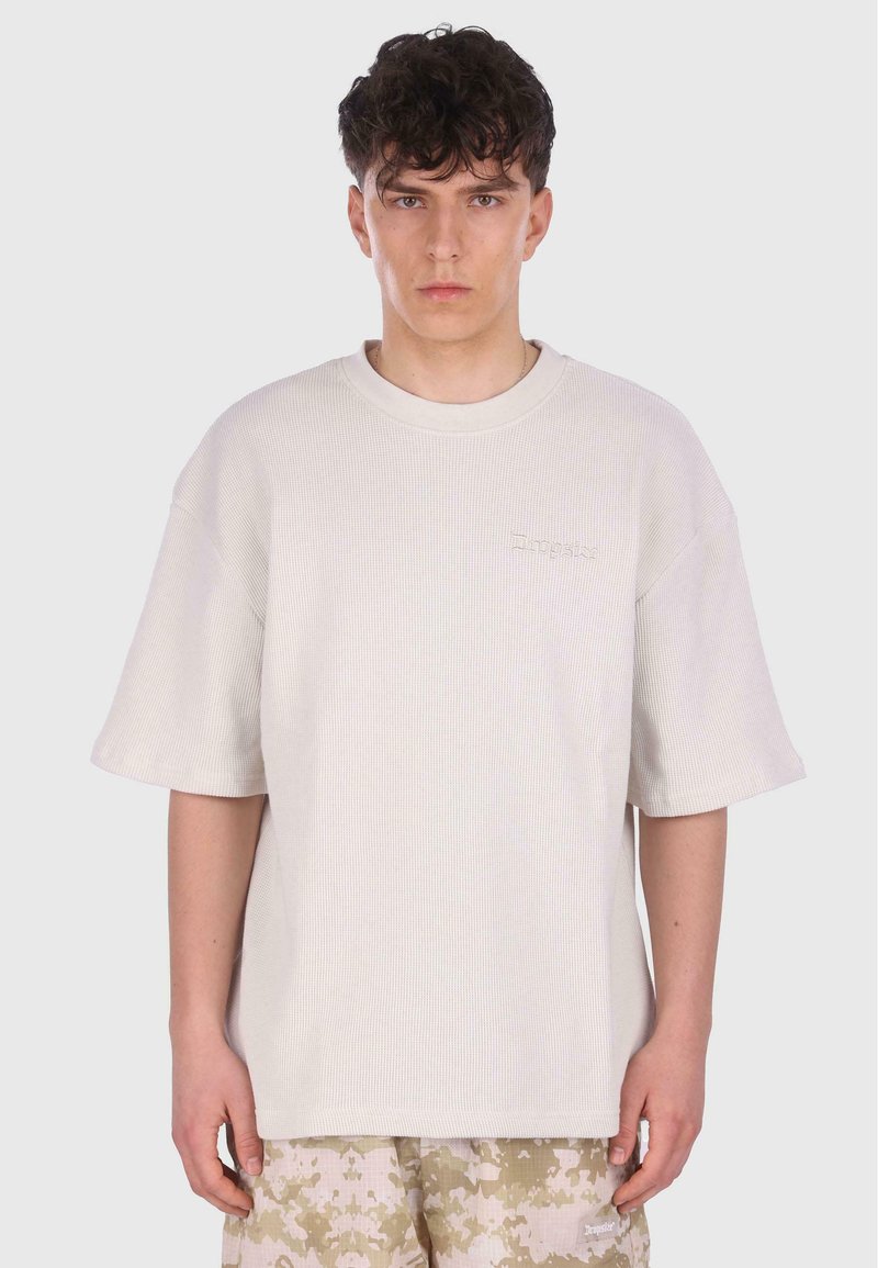 Overdimensioneret cremefarvet ribbede bomulds T-shirt med korte ærmer, prydet med et diskret broderet logo på brystet og en afslappet pasform.