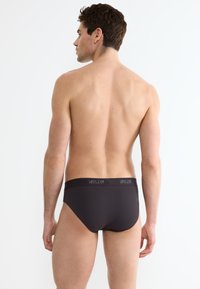 Slip neri scuri con una texture liscia, caratterizzati da un elastico con logo. Il design è minimalista, senza ulteriori motivi o accenti.