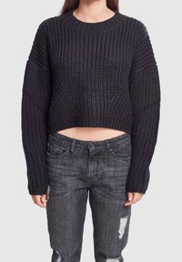 Maglione corto nero a maglia con collo a coste e maniche larghe, abbinato a jeans grigi strappati con chiusura a bottone e tasche.