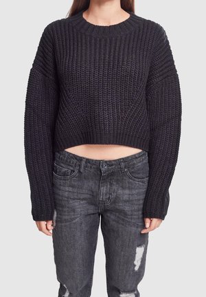 Zwart gebreid crop sweater met een geribde halslijn en wijde mouwen, gecombineerd met versleten grijze jeans met een knoopsluiting en zakken.