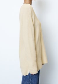 Pull beige en tricot avec une coupe décontractée, doté d'un col rond, de manches longues, d'ouvertures sur les côtés et de poignets côtelés.