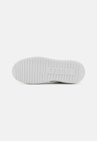 Semelle de chaussure en caoutchouc blanc avec texture côtelée et logo "Guess" embossé. Forme arrondie avec bords sans coutures pour un design minimaliste.