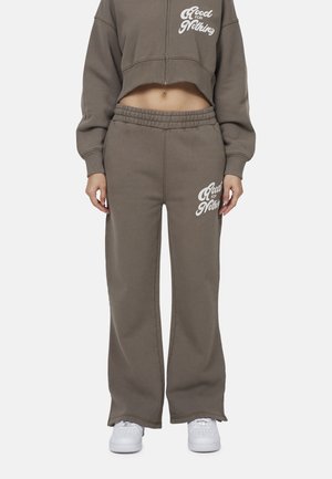 Felpa corta di colore marrone opaco abbinata a pantaloni della tuta con cintura elastica. Testo bianco "Good for Nothing" sui pantaloni. Sneakers bianche.