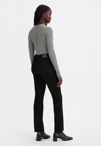 Camisa de manga larga a rayas con un diseño ajustado, combinada con unos vaqueros de campana negros que tienen un acabado texturizado y detalles en los bolsillos traseros.