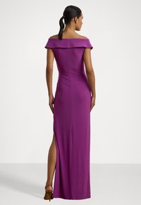 Vestido roxo com decote caído, silhueta ajustada, fenda lateral e tecido suave. Apresenta um decote mais discreto e um design minimalista.