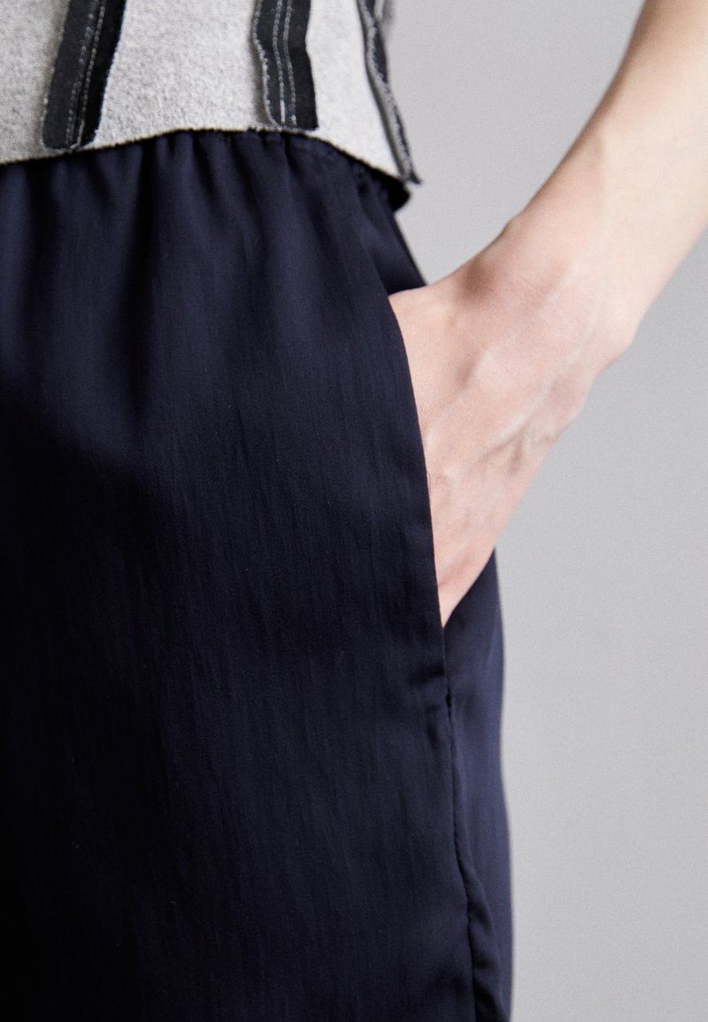 Marineblaue, leichte Hose mit glatter Textur. Verfügt über eine Seitentasche und eine lockere Passform, kombiniert mit einem grauen Oberteil mit schwarzen vertikalen Streifen.