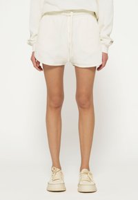 Pantaloni corti bianchi e morbidi con vita regolabile e texture soffice, caratterizzati da un orlo arrotondato e abbinati a sneaker di colore chiaro.