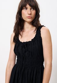Schwarzes Kleid aus strukturiertem, gewelltem Stoff, mit einem gerafften Ausschnitt und verstellbaren Bändern, sowie einer taillierten Taille und einem fließenden Rock.