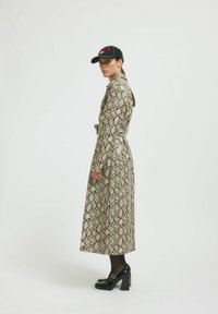 Dolga, plaščastega vzorca v bež in črni barvi, z obdelanim pasom, dolgimi rokavi in stransko odprtino, v kombinaciji s črnimi kapicami in masivnimi petami.