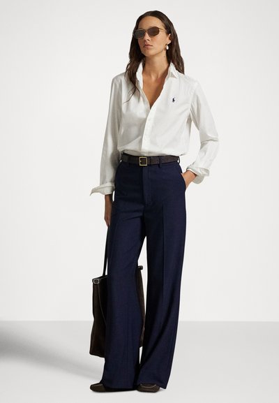 Camisa branca de botões, calças largas escuras, cinto castanho, mala castanha, óculos de sol. Tecido liso, design clássico, ajustado nos ombros, corte relaxado.