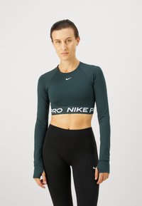 Ciemnozielony krótki top z długim rękawem z białym nadrukiem "PRO" oraz bandą z logo "NIKE". W połączeniu z czarnymi legginsami z wysokim stanem. Gładka, dopasowana struktura.