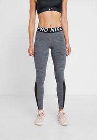 Soutien-gorge de sport noir associé à un legging gris avec une finition texturée, des panneaux latéraux en mesh noir et une ceinture élastique "PRO NIKE".