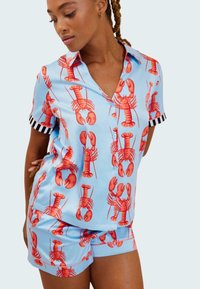 Conjunto de pijama de manga corta, color azul claro, con grandes estampados de langosta roja, y detalles a rayas en negro y blanco en las mangas. Textura de tela suave.