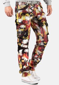 Pantalons cargo avec un motif éclaboussures de peinture multicolore, dotés de zips, d'étoiles et de poches ; fabriqués en denim avec une coupe décontractée et une jambe fuselée.