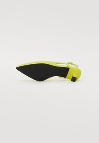 Chaussure à talons aiguilles de couleur jaune fluo avec un bout pointu, offrant une finition brillante et une semelle extérieure noire, agrémentée d'une sangle avec boucle.