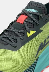 Scarpa sportiva con una tomaia in rete nera e accenti verdi e turchesi, con un passante per i lacci rosso e una suola texturizzata con strisce nere.