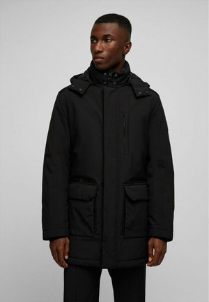 Parka noire et isolée avec un col haut, une capuche ajustable et plusieurs poches avant. Présente une texture lisse et mate ainsi qu'une fermeture éclair à l'avant.